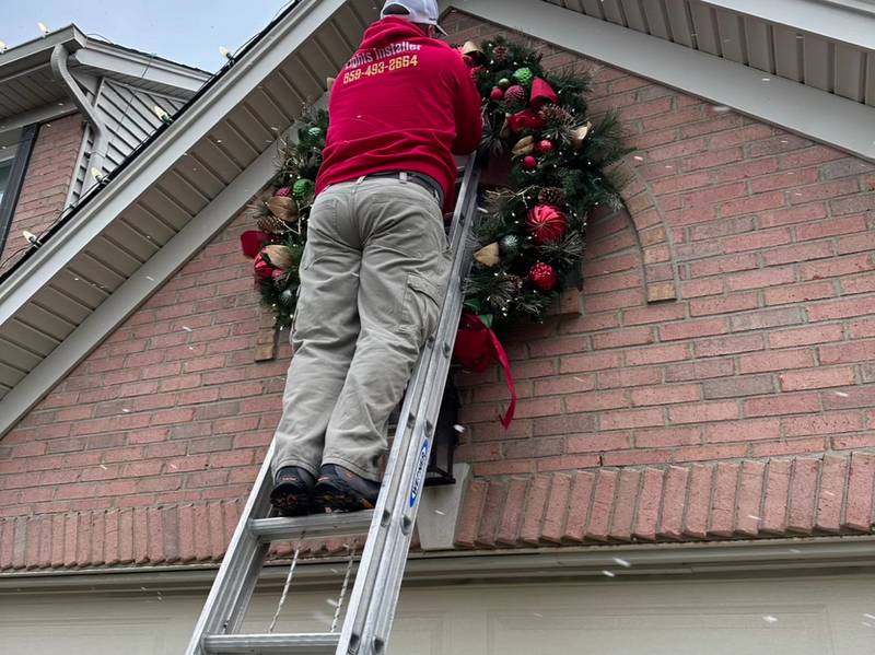 Crew member on a ladder hanging a lit wreath above a garage