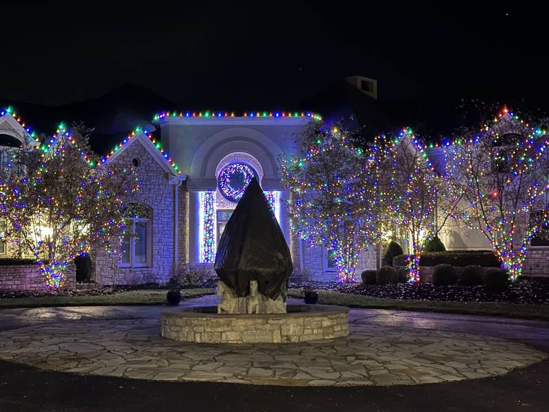 Large home with multicolor roofline lights and lit trees across the front yard