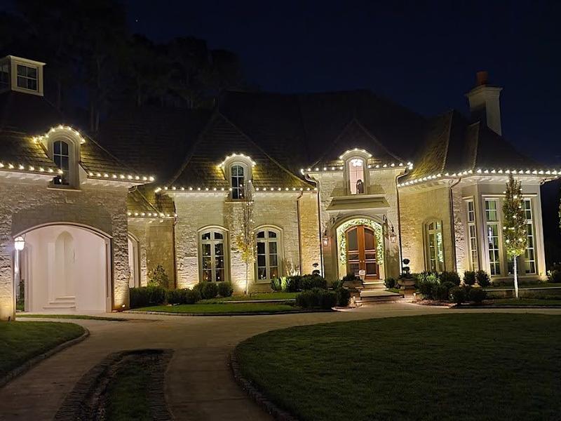 Stone home with warm white lights on the roofline and windows